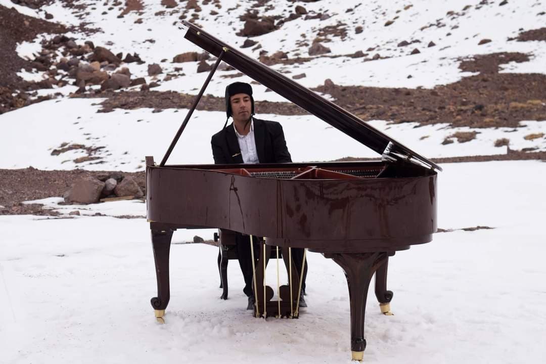 Juan Estay playing a grand piano on snow-covered mountain landscape