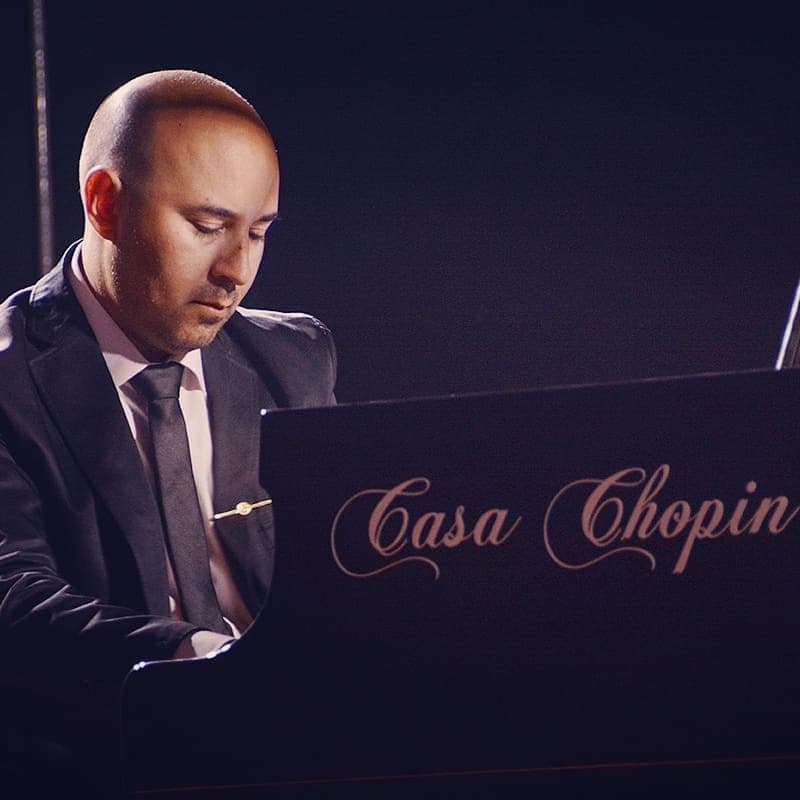 Juan Estay playing at the Casa Chopin piano in dark atmospheric lighting